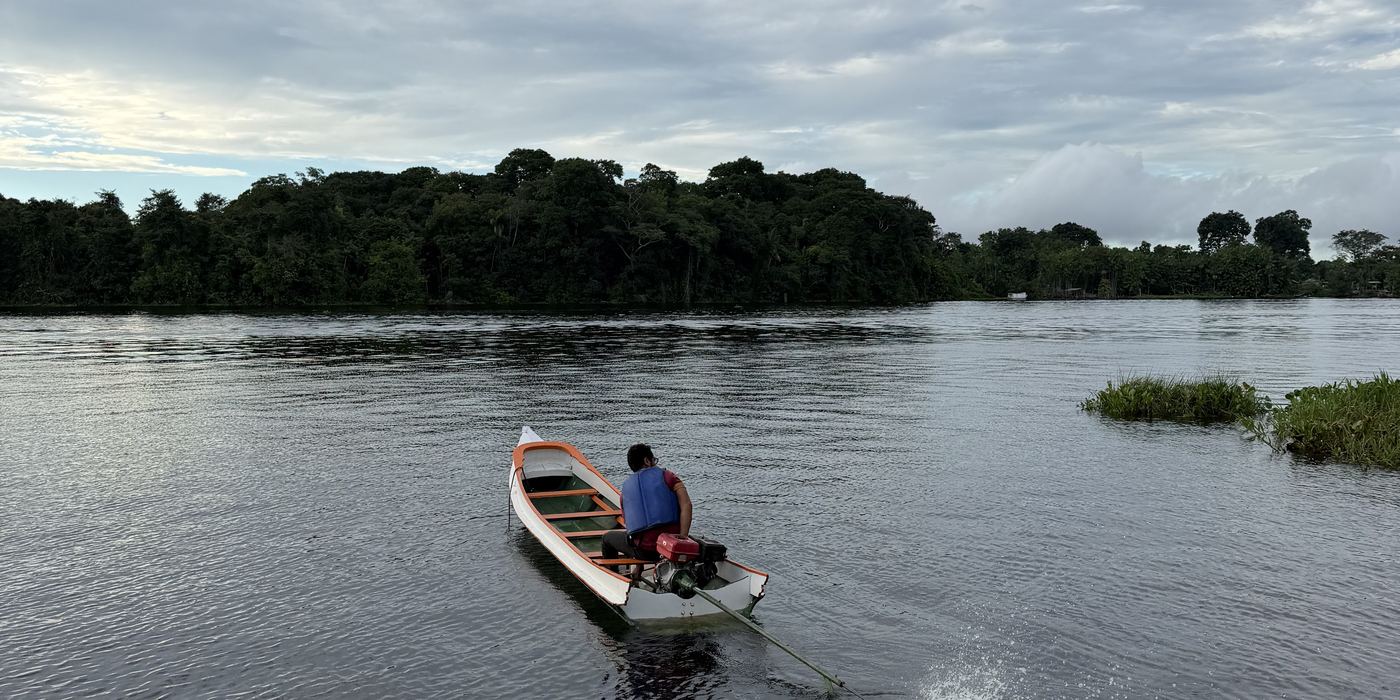 Uma pessoa conduzindo a pequena embarcação no rio largo, sob céu carregado